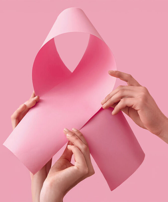 Zwei Hände halten ein rosa Papier, das zu einer Schleife geformt ist, vor einem pinken Hintergrund.