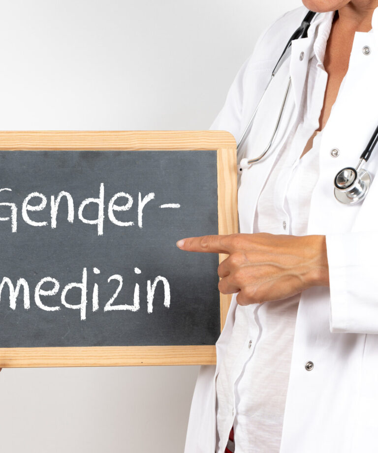 Eine Person in Arztkleidung hält eine Tafel mit der Aufschrift "Gendermedizin".