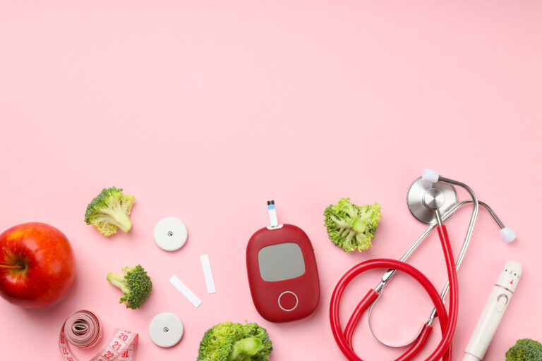 Gesunde Lebensmittel und medizinische Geräte auf rosa Hintergrund, darunter Apfel, Brokkoli, Blutzuckermessgerät und Stethoskop.