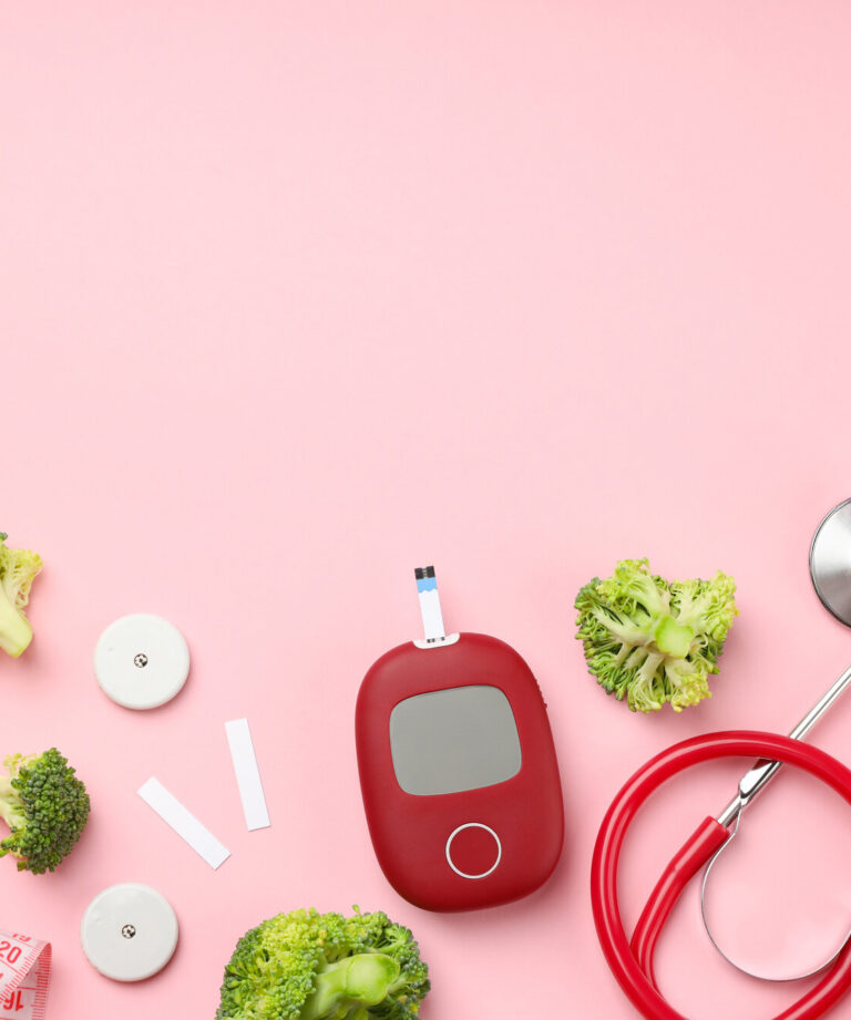 Gesunde Lebensmittel und medizinische Geräte auf rosa Hintergrund, darunter Apfel, Brokkoli, Blutzuckermessgerät und Stethoskop.